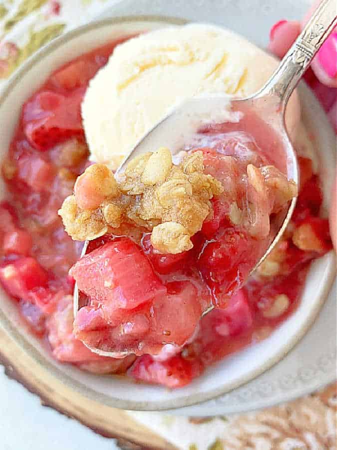 eating a spoonful of warm strawberry rhubarb crisp topped with a scoop of vanilla ice cream