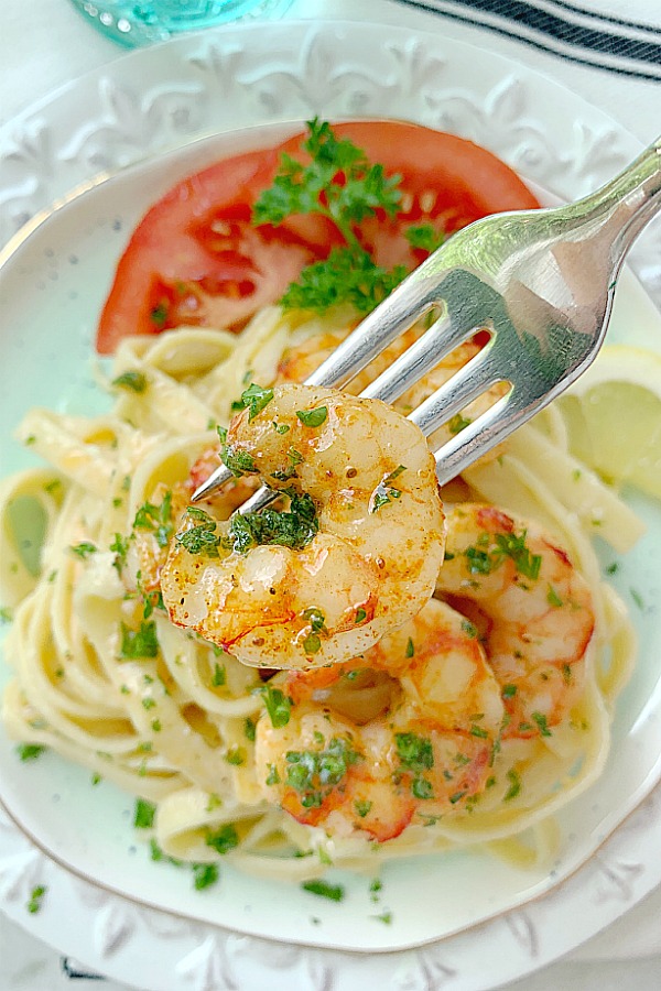 air fryer shrimp on fork over plate of fettuccine alfredo