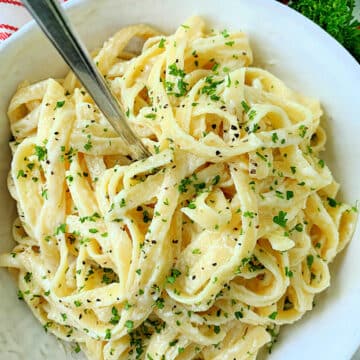 white bowl of fettuccine alfredo garnished with fresh parsley