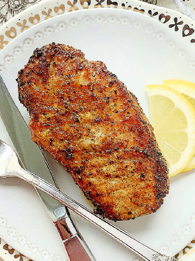 a perfectly air fried pork chop on a plate and garnished with lemon slices