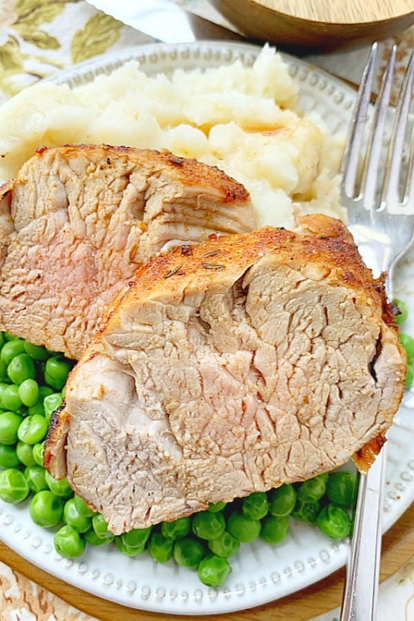 pork tenderloin sliced on a plate with potatoes and peas