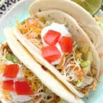 three plated crockpot chicken tacos topped with lettuce, cheese, tomatoes and sour cream