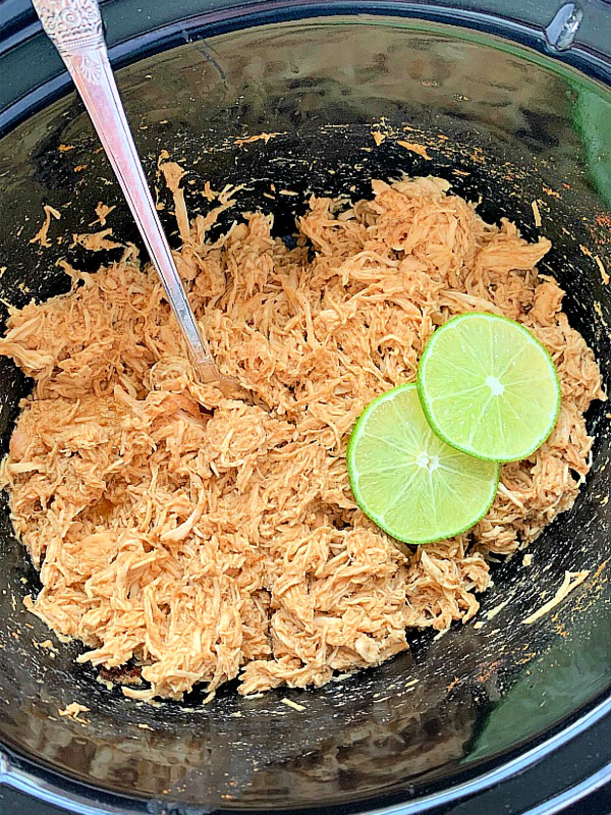 cooked chicken for tacos in the crockpot garnished with a couple of slices of lime