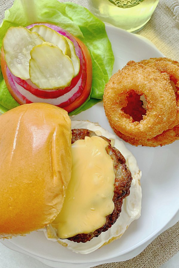 overhead view of burgers on plate with toppings and onion rings