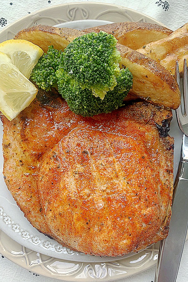 broiled pork chop on a plate with potato wedges