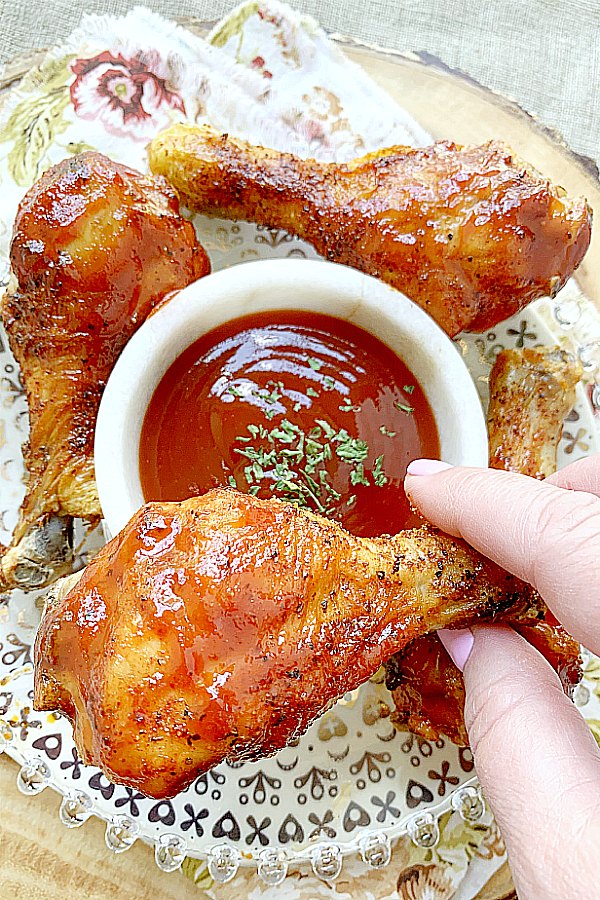 holding an air fryer chicken leg - ready to dip in bbq sauce