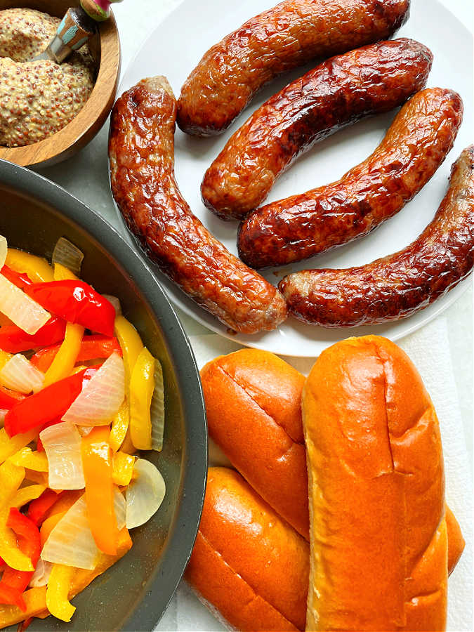 plated air fryer sausage with cooked peppers and onions, buns and mustard