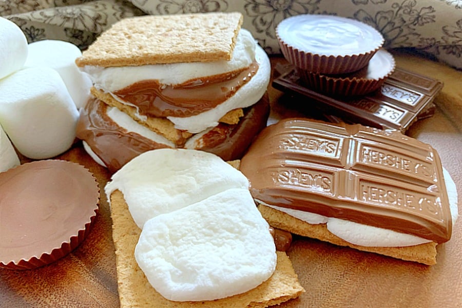 horizontal crop of air fryer s'mores on a platter with stacked chocolate bars, reeses cups and marshmallows