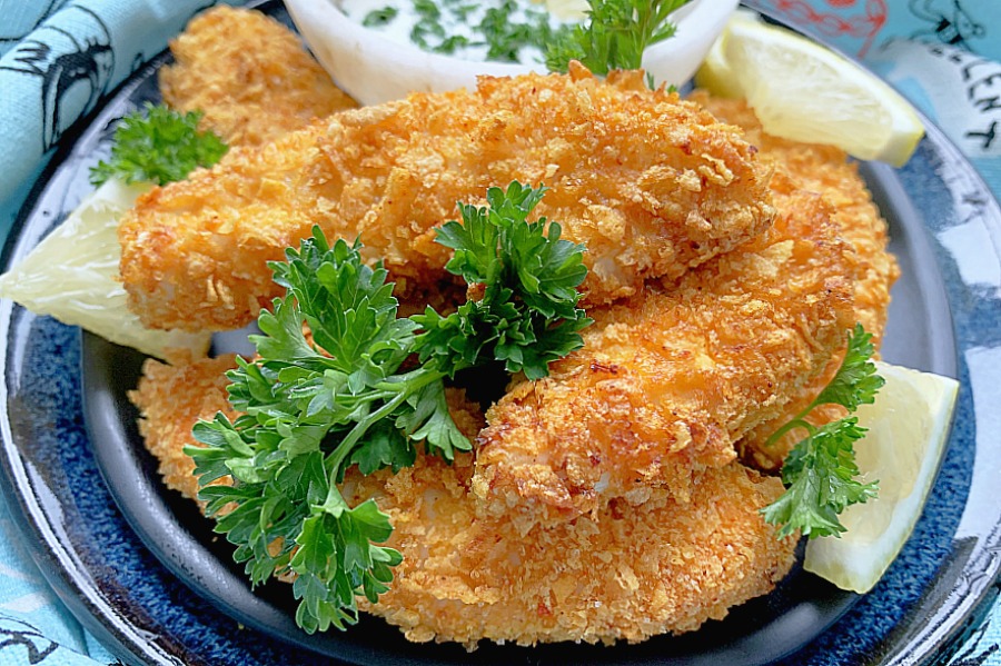 chicken tenders cooked in the air fryer on a plate with lemon slices and fresh parsley for garnish