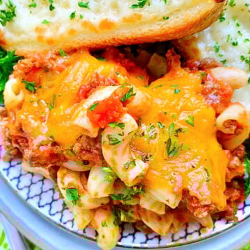 A big serving of Johnny Marzetti casserole on a decorative plate with two slices of cheesy garlic bread