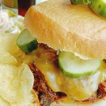 barbecue pulled beef sandwich on a plate with chips and pickles