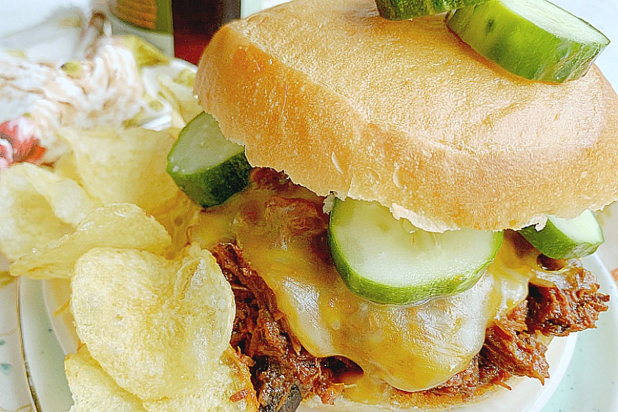 barbecue pulled beef sandwich on a plate with chips and pickles
