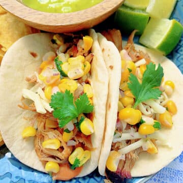 two plated pulled pork tacos topped with corn salsa and garnished with fresh cilantro