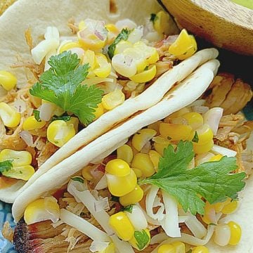 two pulled pork tacos on a plate with chips and guacamole on the side