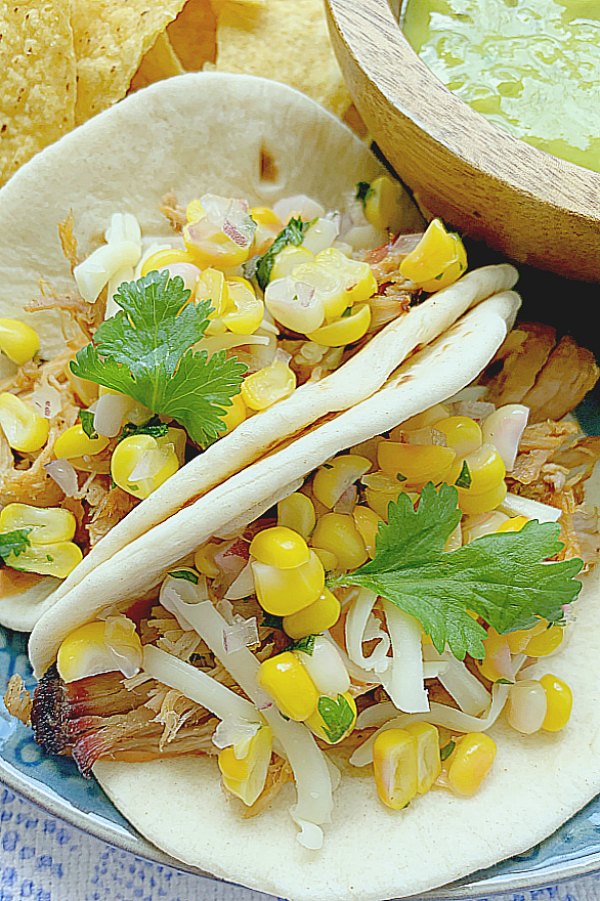 two pulled pork tacos on a plate with chips and guacamole on the side