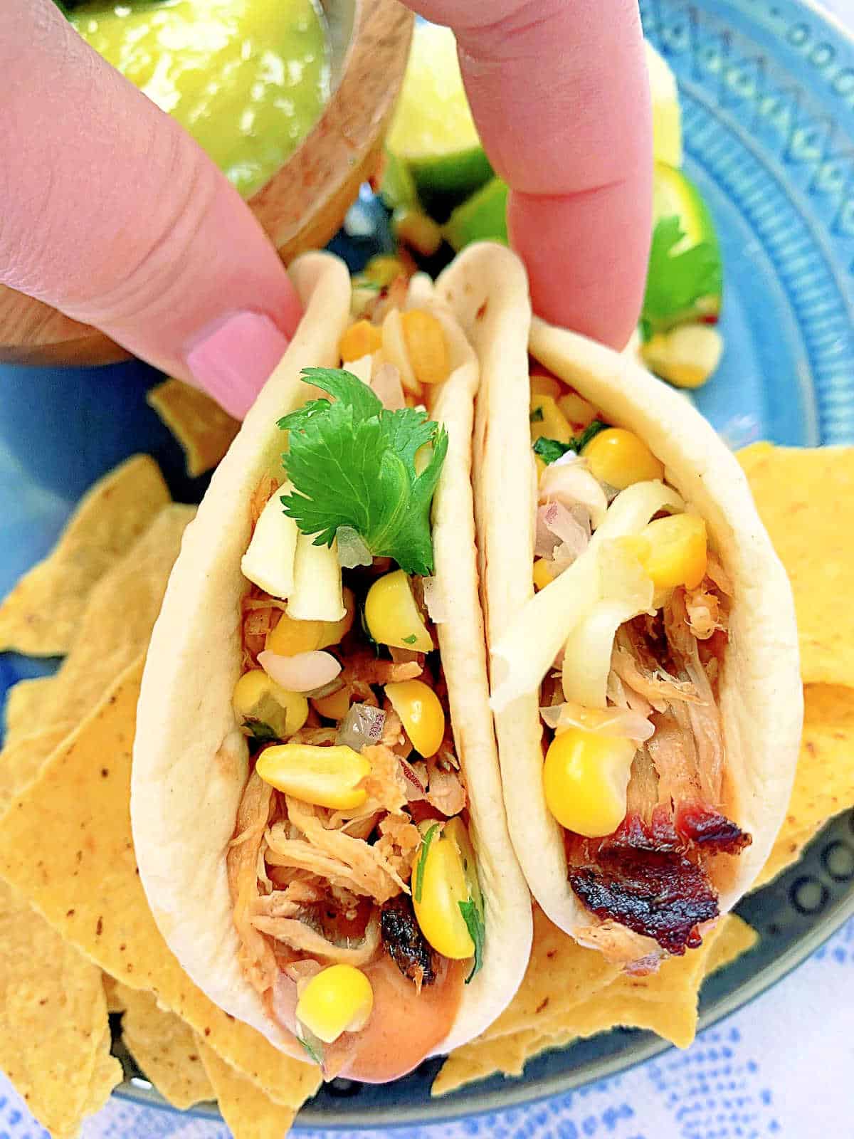 holding up two pulled pork tacos as if ready to take a bite