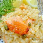 a plate of salmon risotto with fresh dill and lemon slices on the side