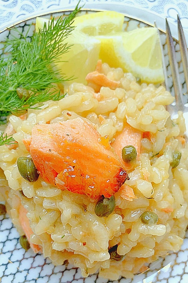 a plate of salmon risotto with fresh dill and lemon slices on the side