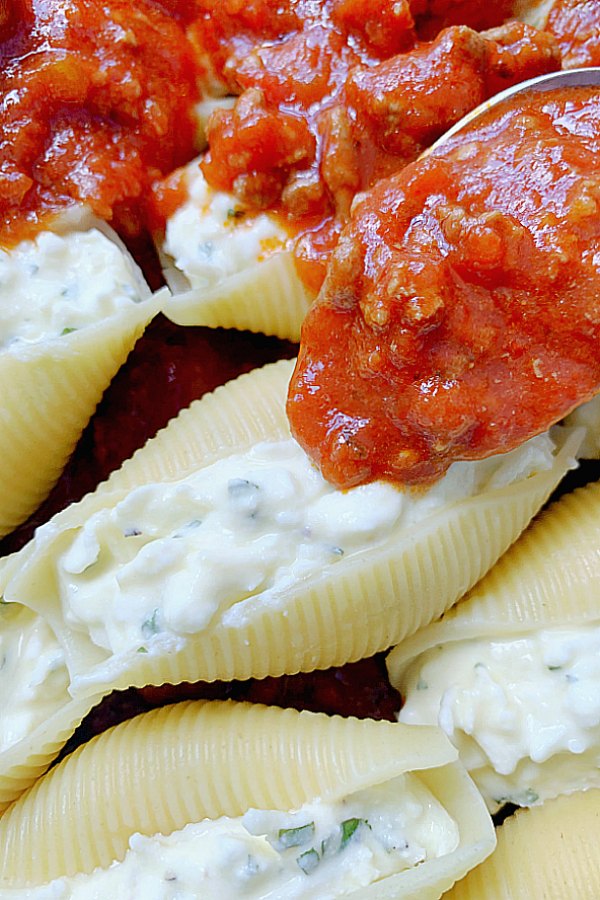 spooning meat sauce onto cheese stuffed shells