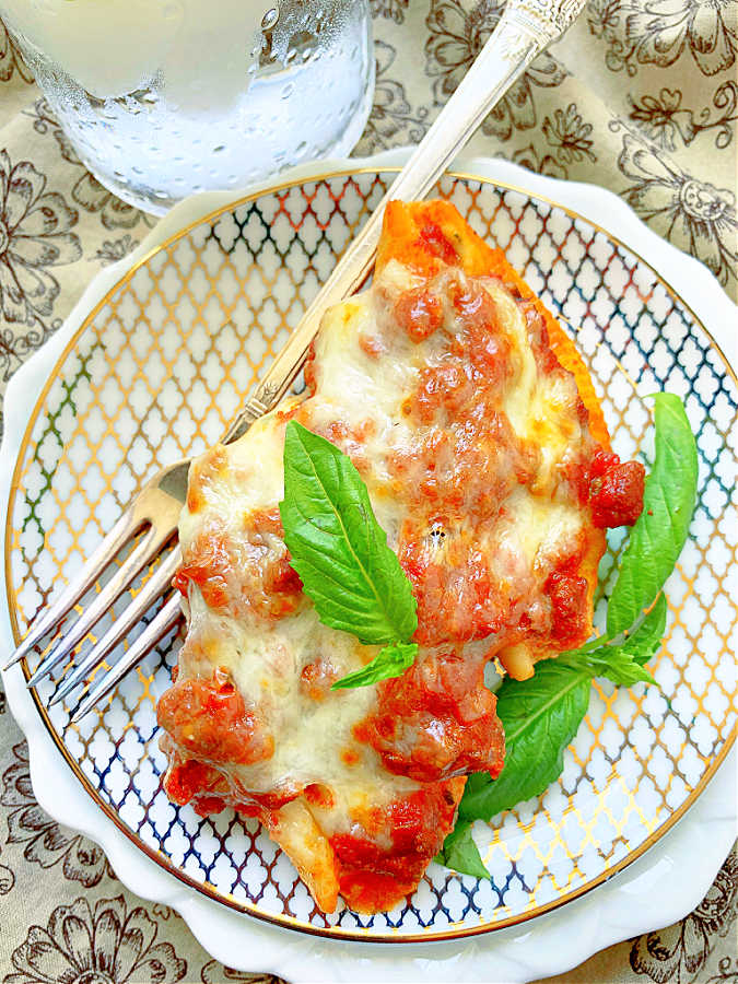 a small serving dish of two Conchiglioni Pasta stuffed shells topped with meat sauce, ready to eat