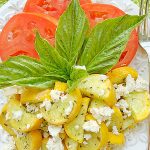 yellow squash topped with feta on a plate with sliced tomatoes and fresh basil