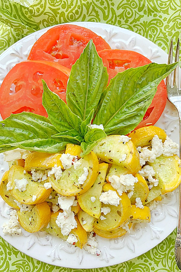 yellow squash topped with feta on a plate with sliced tomatoes and fresh basil