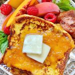 buttermilk french toast on a plate with peaches, raspberries and sausage