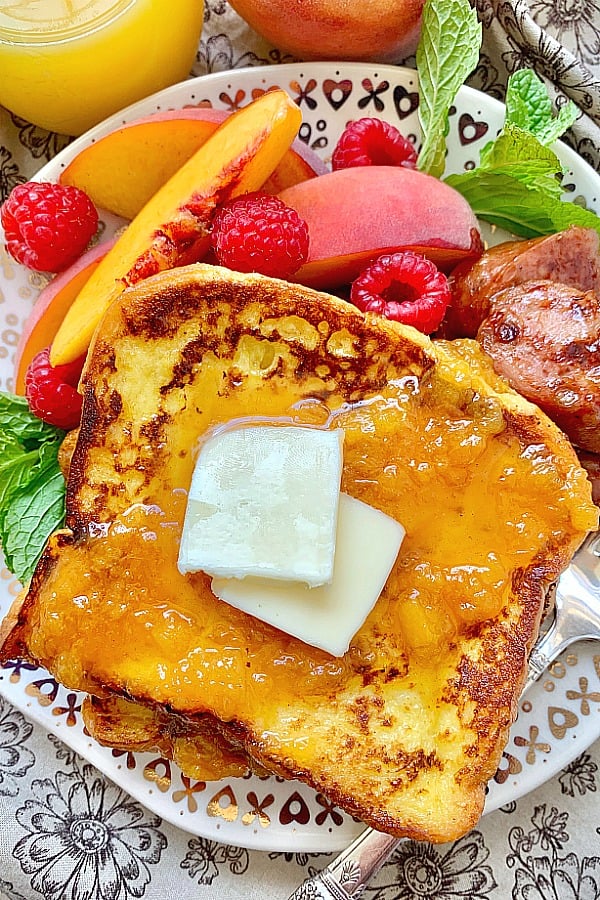 buttermilk french toast on a plate with peaches, raspberries and sausage