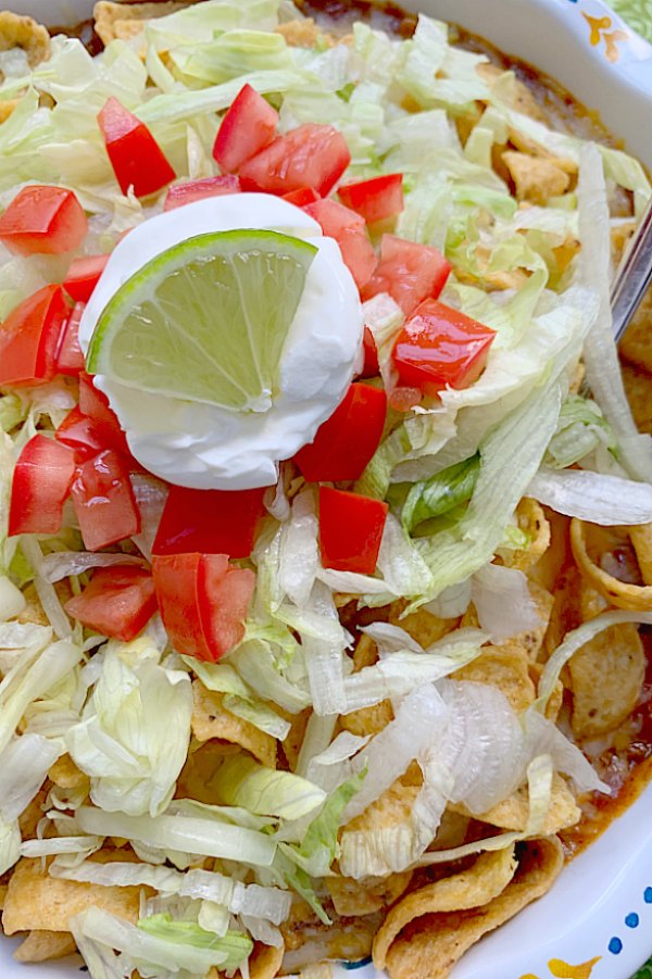 close up view of frito pie topped with lettuce, tomato and sour cream