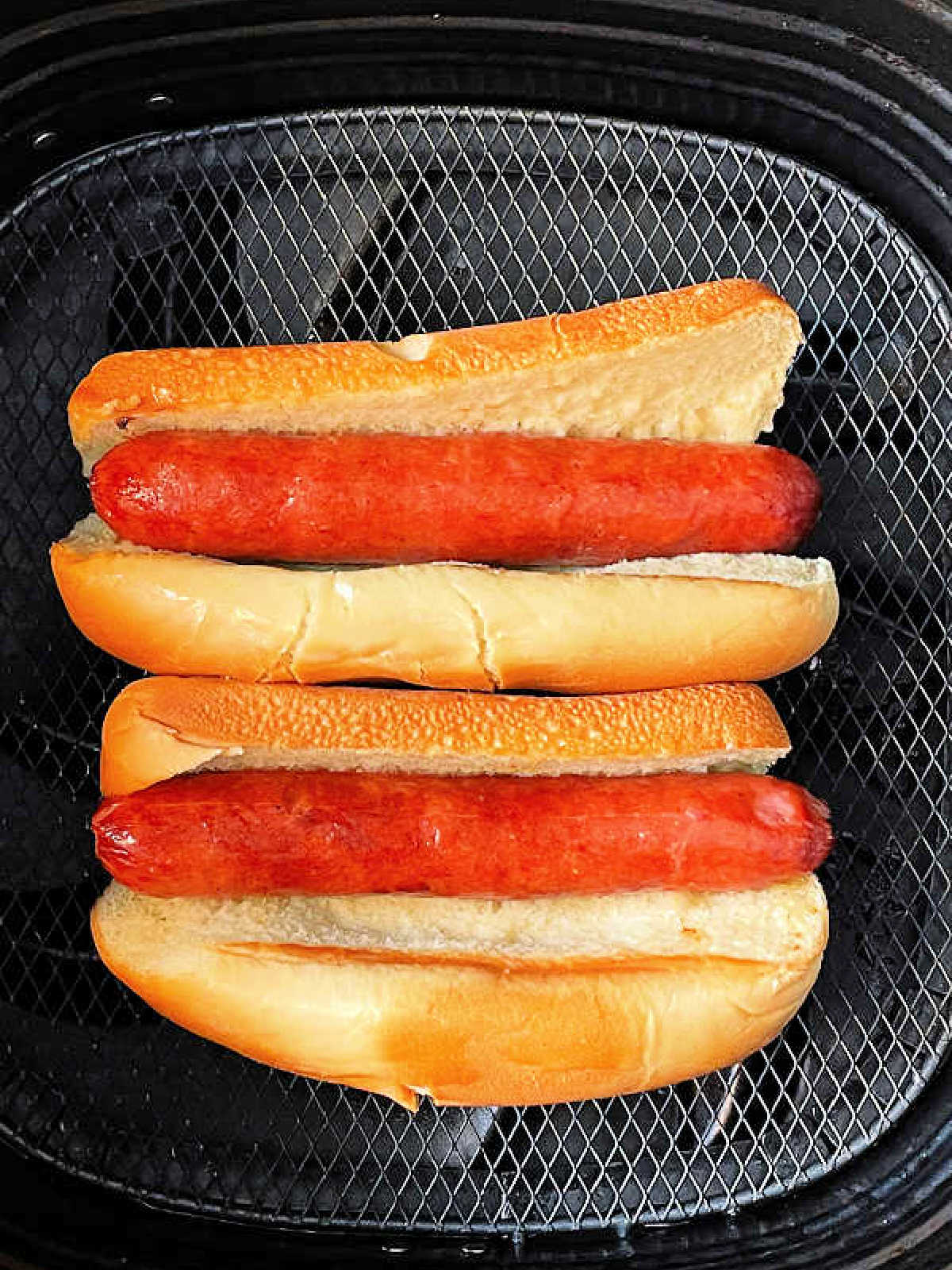 two cooked hot dogs in toasted buns in the air fryer basket