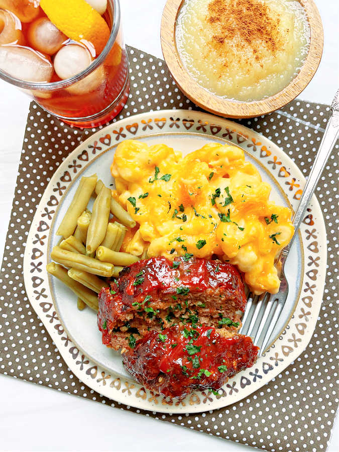 air fryer meatloaf plated with macaroni and cheese and green beans with a side dish of applesauce and iced tea to drink