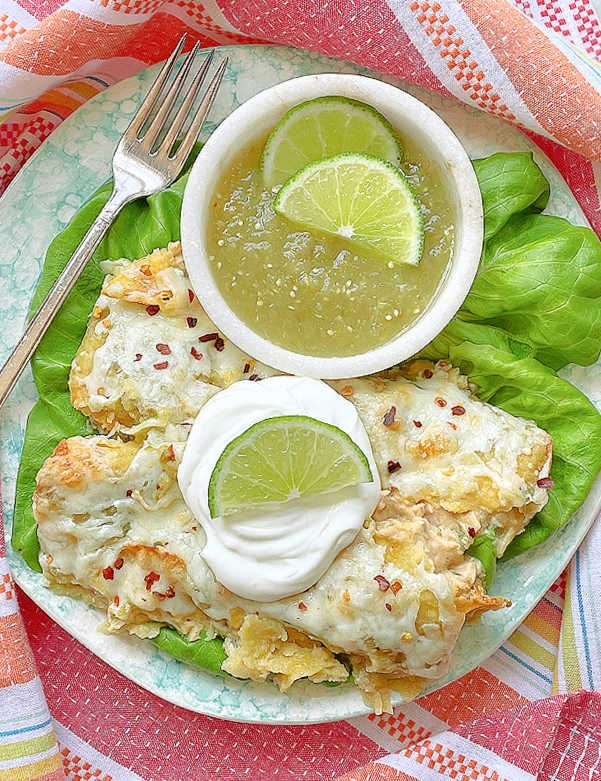 green chicken enchiladas on a plate topped with sour cream