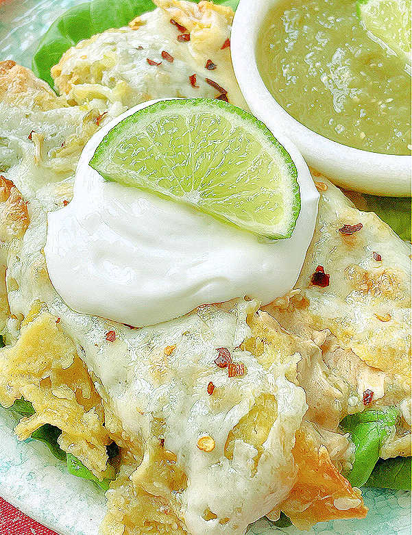 close up photo of green chicken enchiladas topped with sour cream and salsa on the side