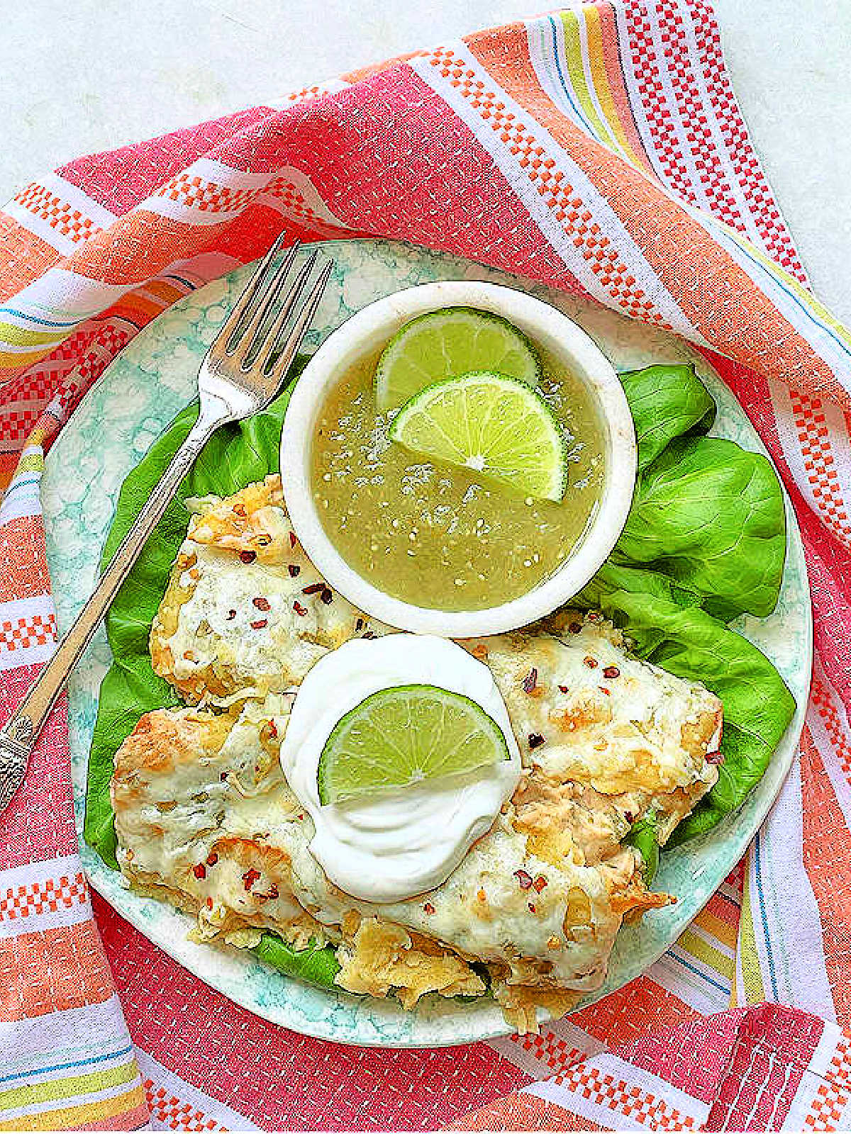 plated green chicken enchiladas on a bed of lettuce with a bowl of green salsa