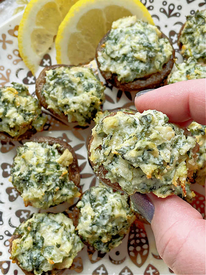 picking up a spinach and artichoke stuffed mushroom to take a bite