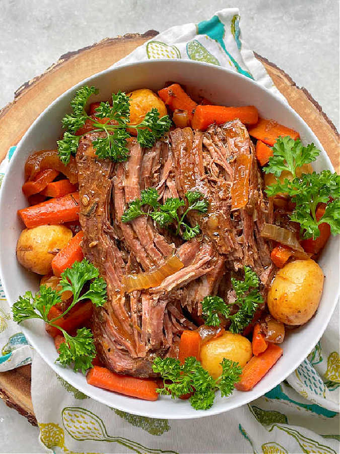 sirloin tip post roast plated with potatoes and carrots and garnished with sprigs of fresh parsley