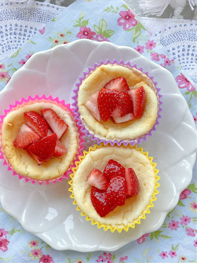 three air fryer cheesecakes on a plate topped with fresh strawberries