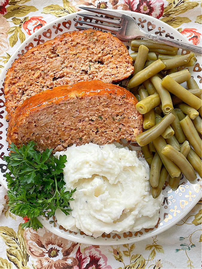 a plate filled with slices of ham loaf, potatoes and green beans