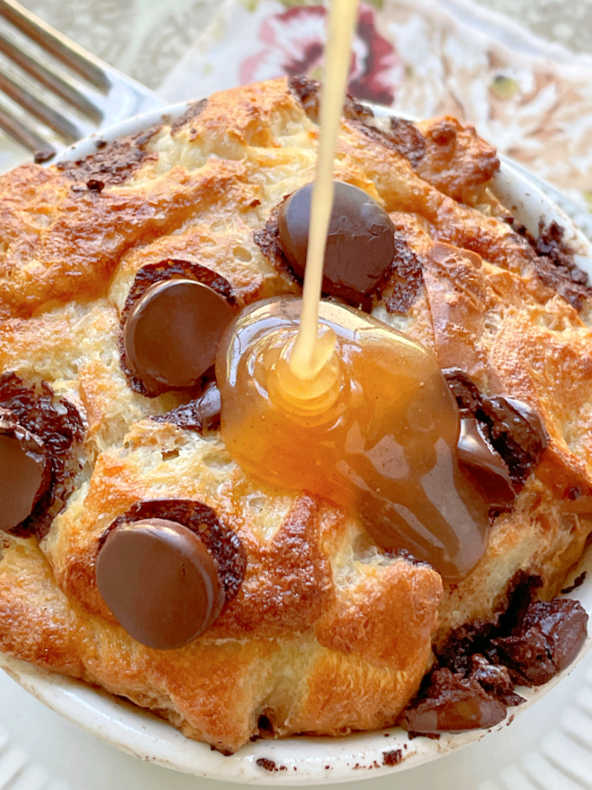 pouring the bourbon butter sauce over the air fryer bread pudding in a ramekin dish