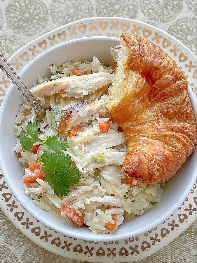 creamy chicken risoni in a bowl with a croissant on the side