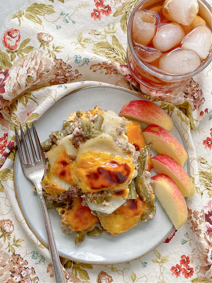 hamburger potato casserole on a plate with apple slices and iced tea