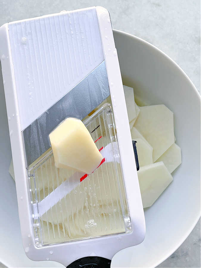 potatoes being sliced with mandolin