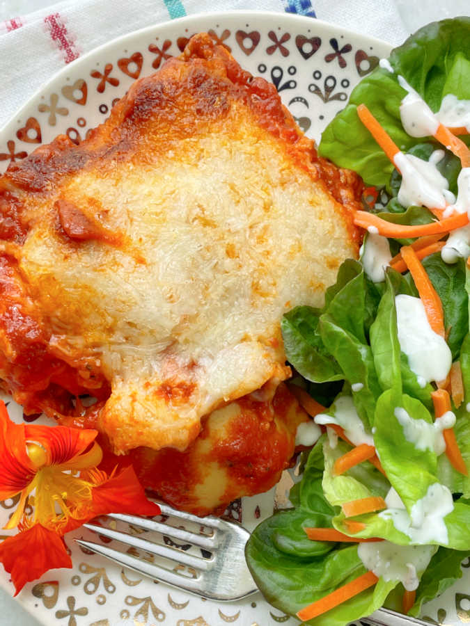 a slice of ravioli lasagna on a plate with tossed salad