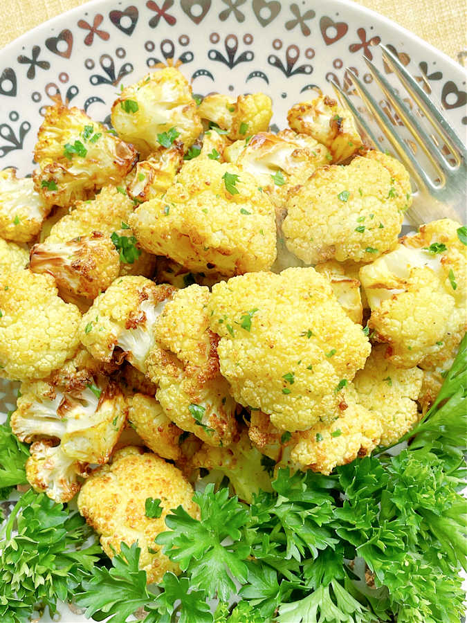 A plate of yellow hued roasted cauliflower fresh from the air fryer ready to eat