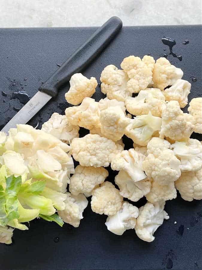 cut up cauliflower florets with knife on a black cutting board