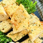 sliced air fryer garlic bread on a cutting board and garnished with fresh parsley and a head of garlic