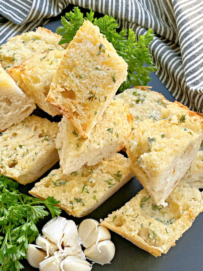 slices of air fryer garlic bread on a cutting board with parsley and garlic garnish