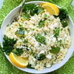 a serving bowl of orzo pasta salad garnished with fresh parsley and lemon wedges
