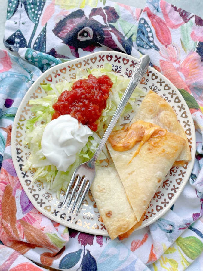 air fryer quesadilla on a plate with a side of lettuce, sour cream and salsa