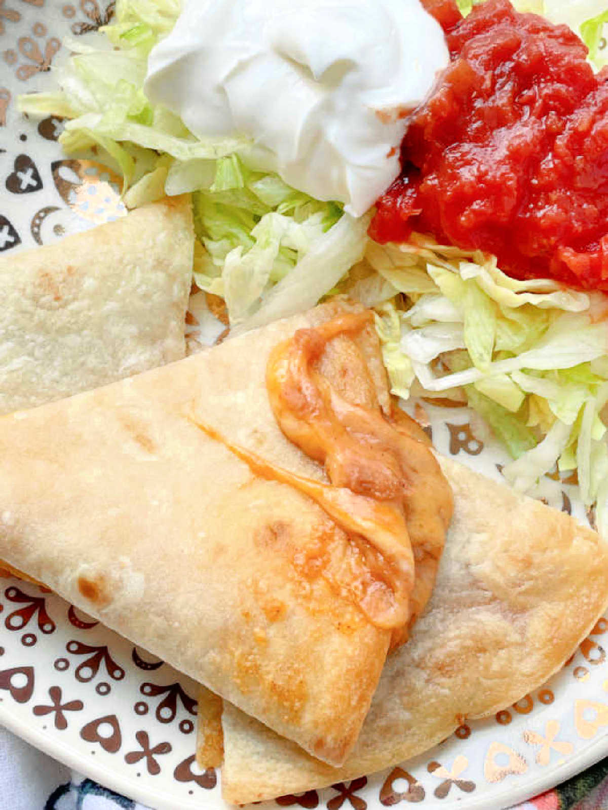 air fryer bean and cheese quesadilla plated with sour cream, lettuce and salsa